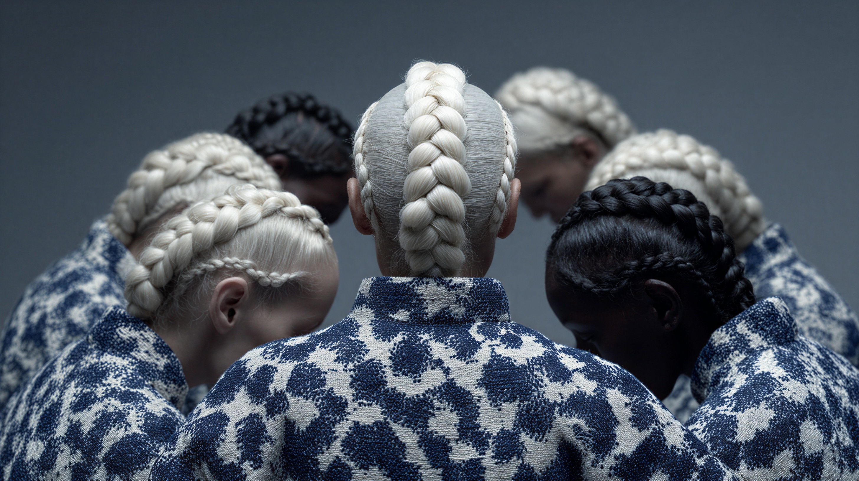 A group of figures seen from behind with elaborate braided hair and blue and white garments